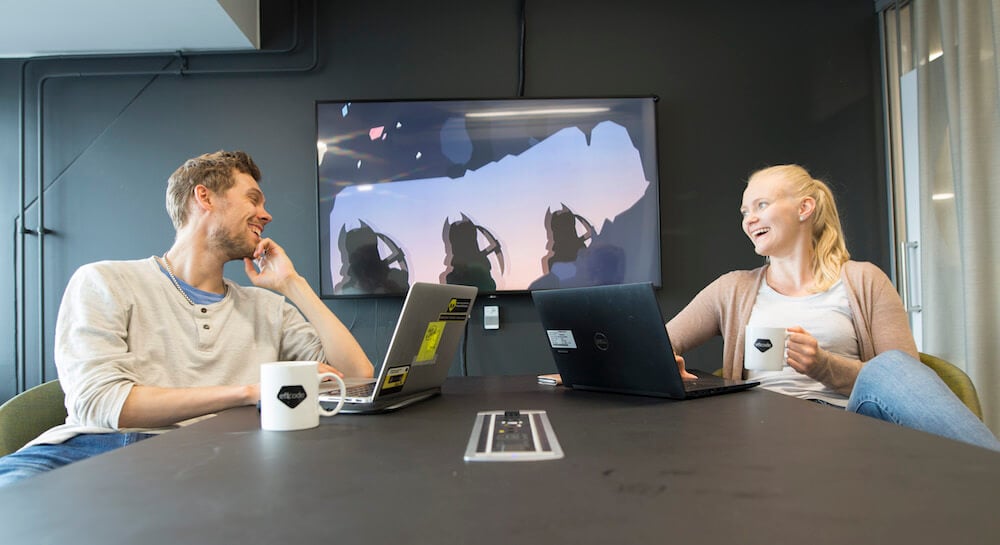 two people sitting by the table at Eficode with computers and mugs