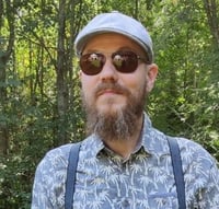 Kuvassa Samu Wikstedt aurinkolasit päässä metsämaisemassa.