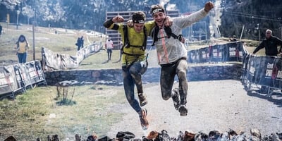 two runners jumping over an obstacles while holding each other