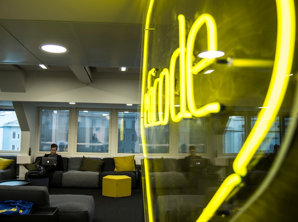 A person reading on a laptop at the eficode office with a large neon eficode logo