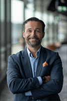 A picture of Jens Skyman, Leader for the Nordic region at HashiCorp, crossing his hands and smiling while wearing a navy blue suit jacket and a blue dress shirt with an orange pocket square.