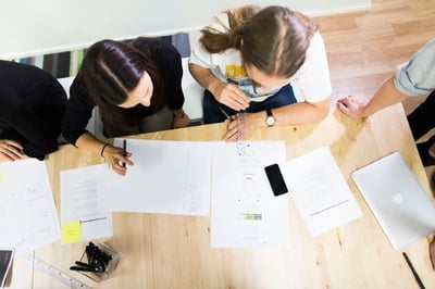 two women sitting by the table having pens and looking at papers at the table